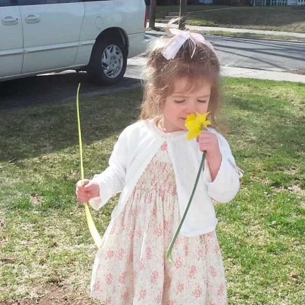 Little girl wearing dress and smelling a flower.