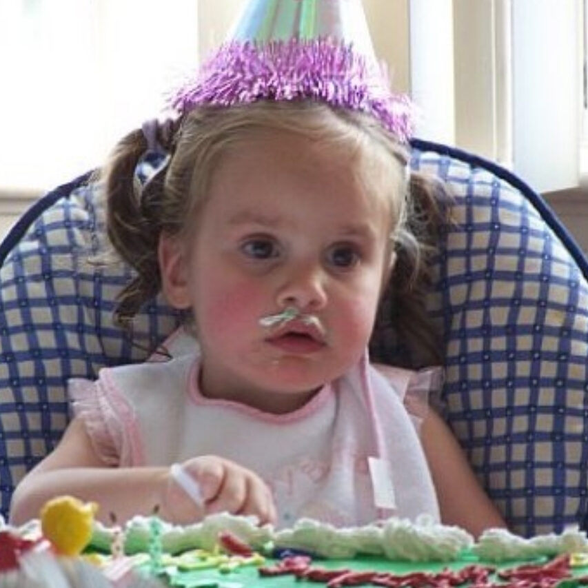 Little girl celebrating a birthday with cake on her face.