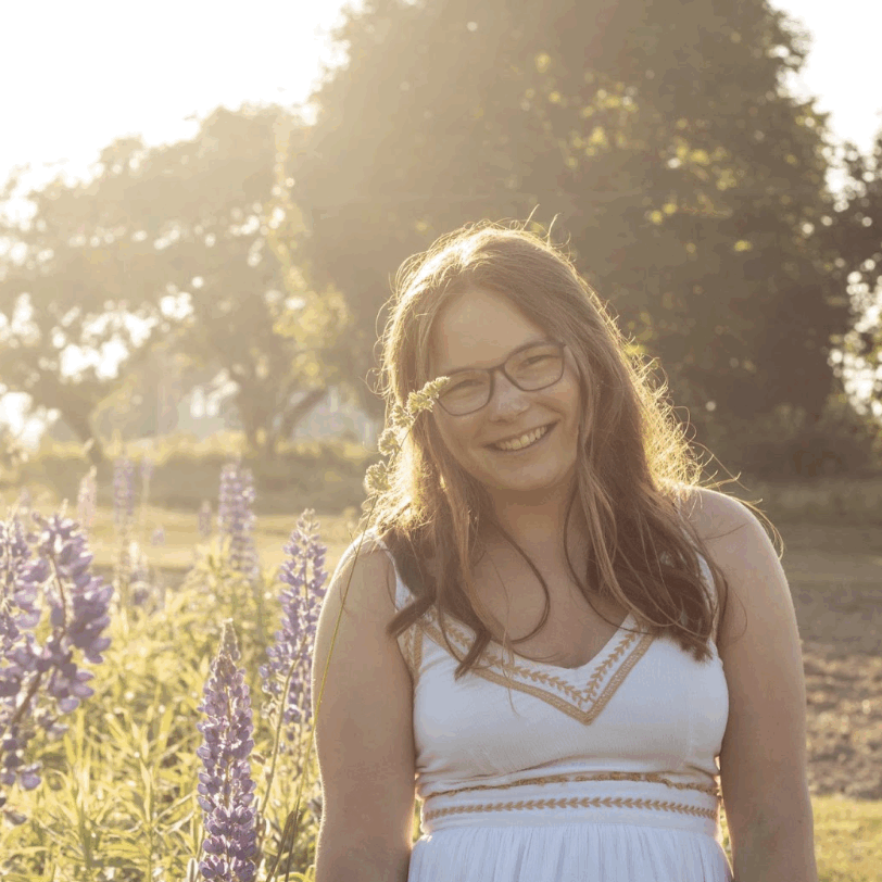College-aged girl posing and smiling amongst lilacs.