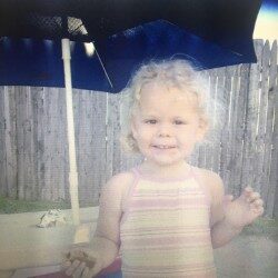 Little girl smiling under an umbrella at the beach.