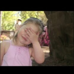 Little girl standing underneath a tree covering her eyes.