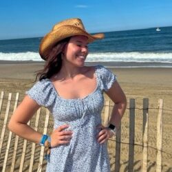 College-aged girl posing in front of the ocean, wearing a cowgirl hat.